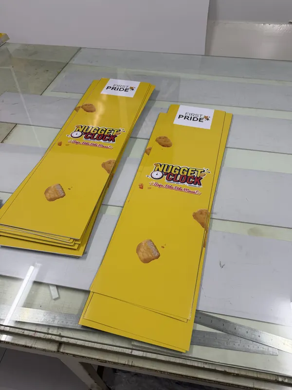 Die-cut printed promo boards, stacked after cutting.